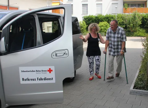 Freiwillige Rotkreuz-Fahrerin holt Fahrgast zu Hause ab und fährt ihn zur Therapie.